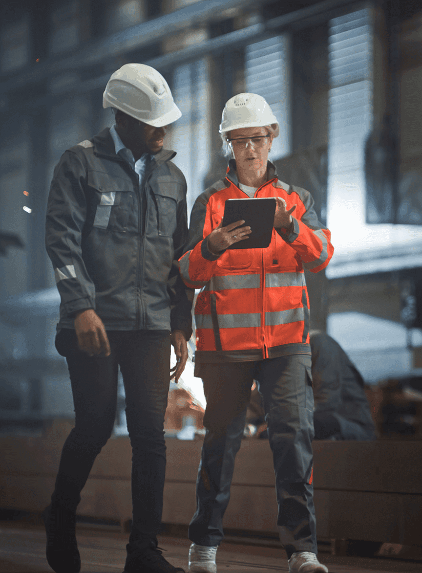 Two heavy industry engineers walk in steel factory use tablet and discuss work industrial worker
